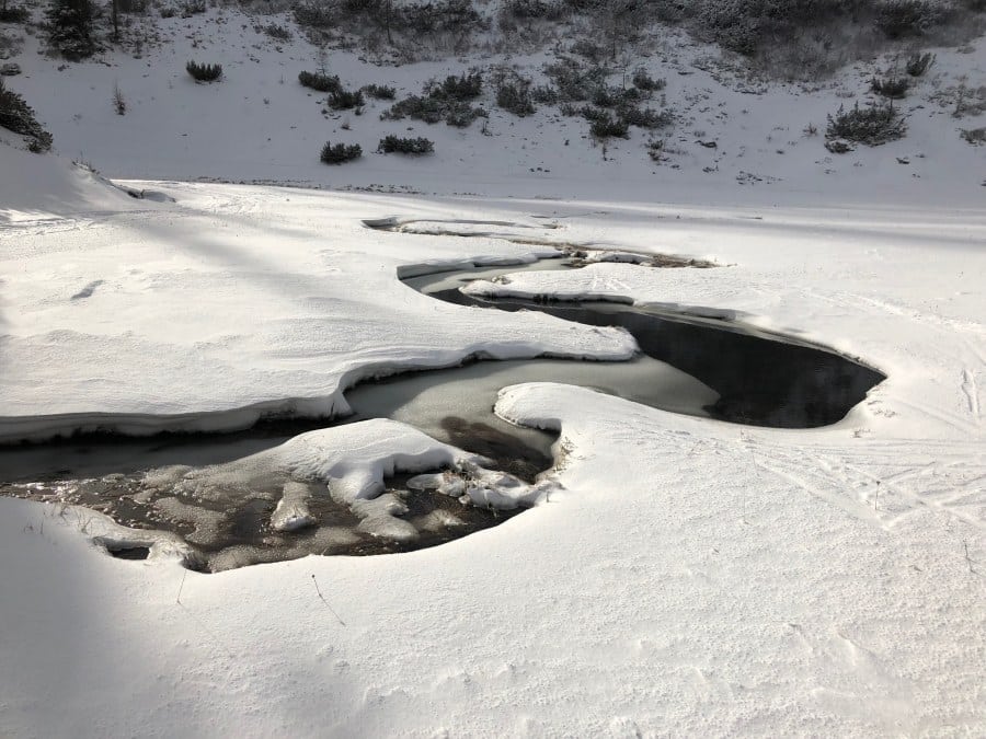 Teilweise zugefrorener Bachlauf in Schneelandschaft